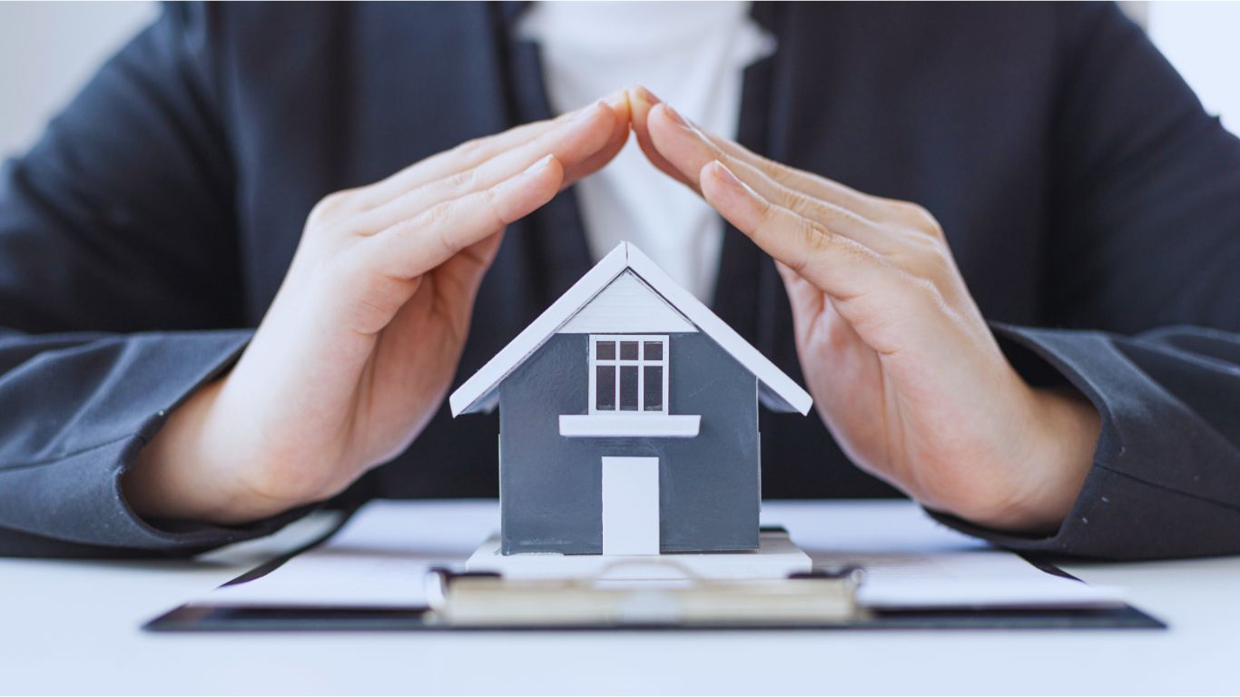 Hands sheltering a model house on property paperwork