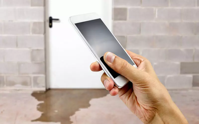 Person using a phone beside water pooling on a floor