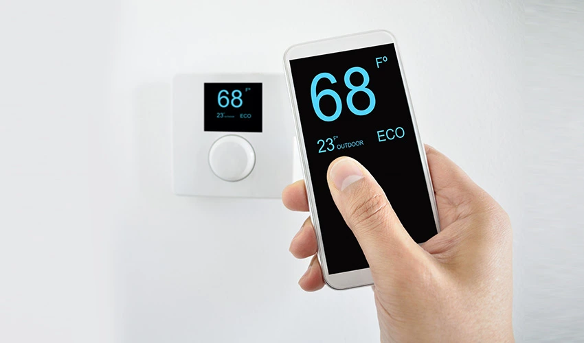 Phone displaying thermostat controls beside a wall thermostat