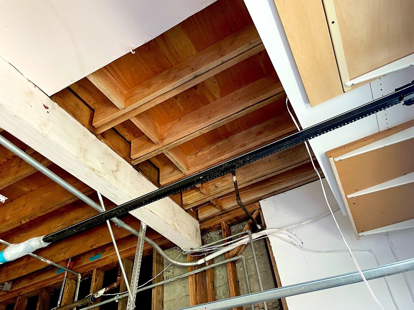 Exposed ceiling joists and plumbing above a kitchen