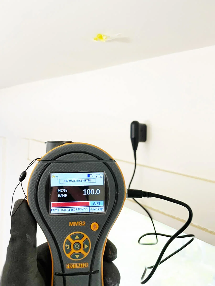Moisture meter checking a wall beneath a marked ceiling — Pacifica, CA