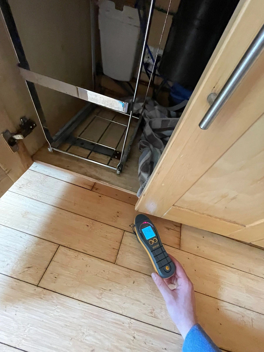 Moisture meter testing flooring beside a refrigerator — San Francisco, CA