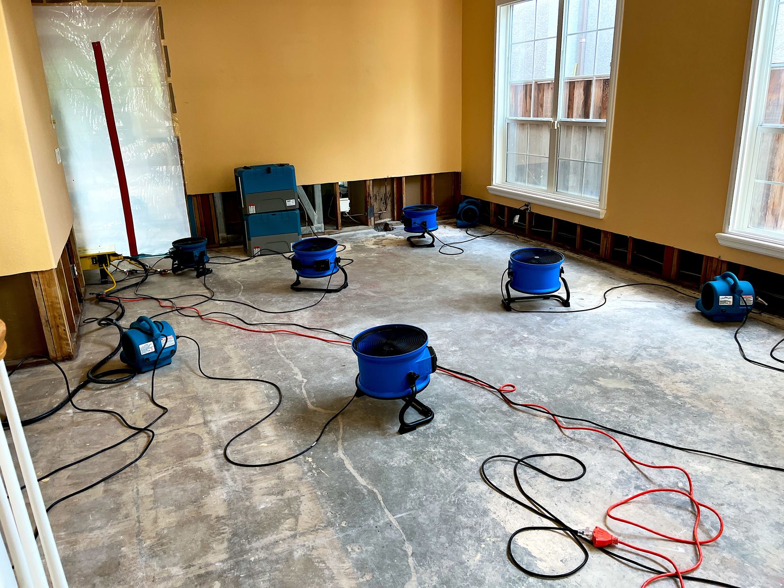 Air movers and a dehumidifier drying a room with exposed subfloor